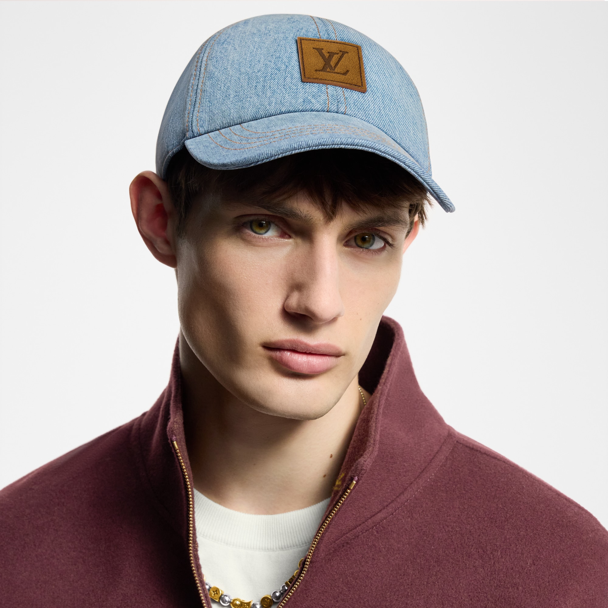 Model wearing a dark denim Louis Vuitton men’s cap with a light neutral jacket.